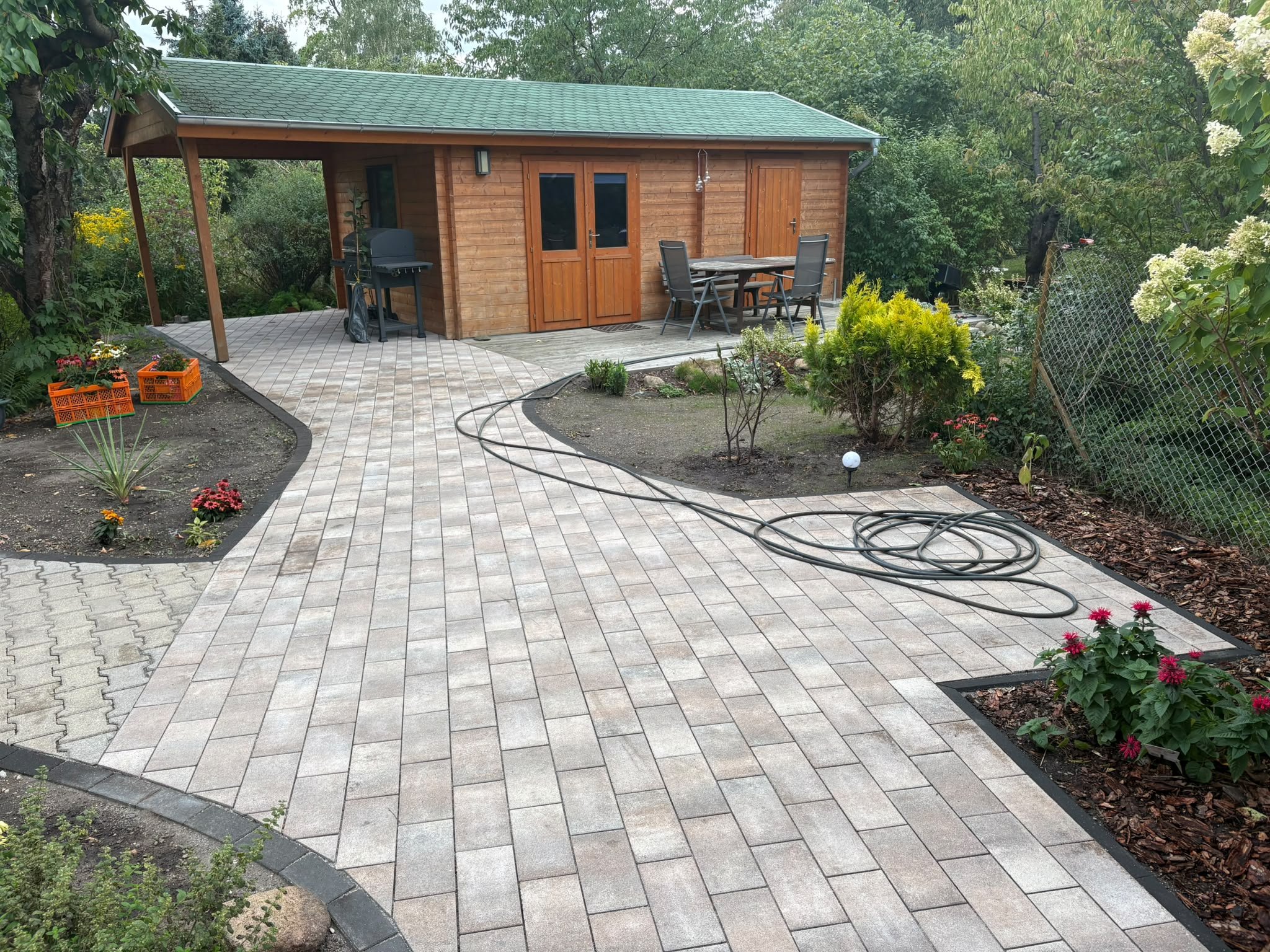Gepflasterter Gartenweg mit Beeten und Rosen, der zu einem Gartenhaus mit Terrasse führt