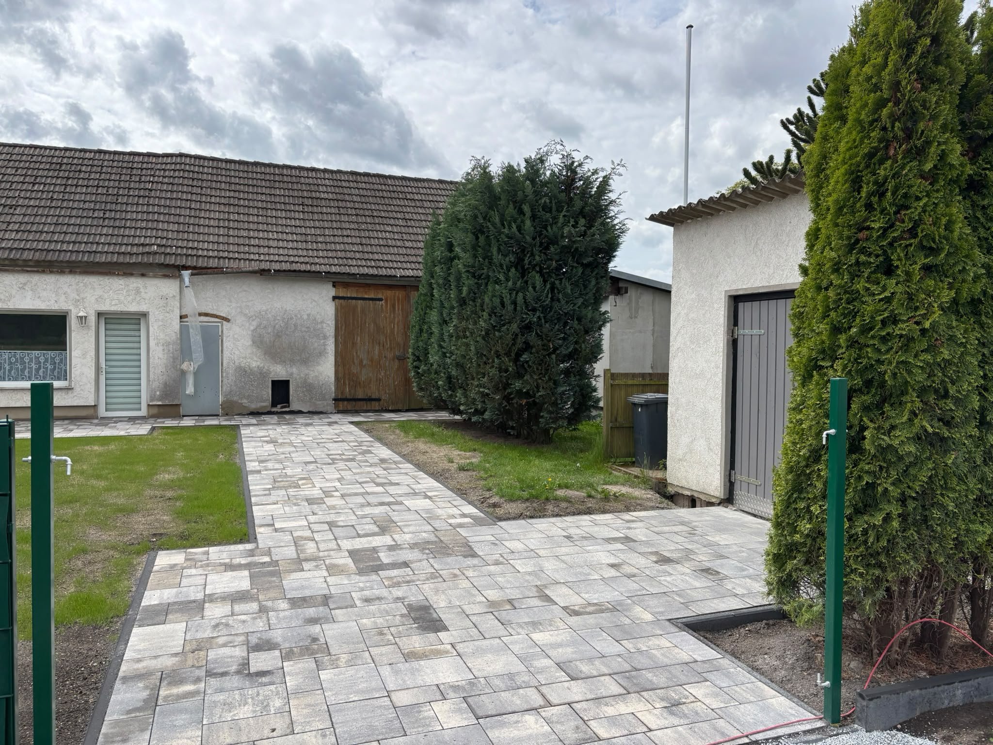 Neuer Rasen und Pflasterweg im Hof, eingefasst von einem grünen Zaun