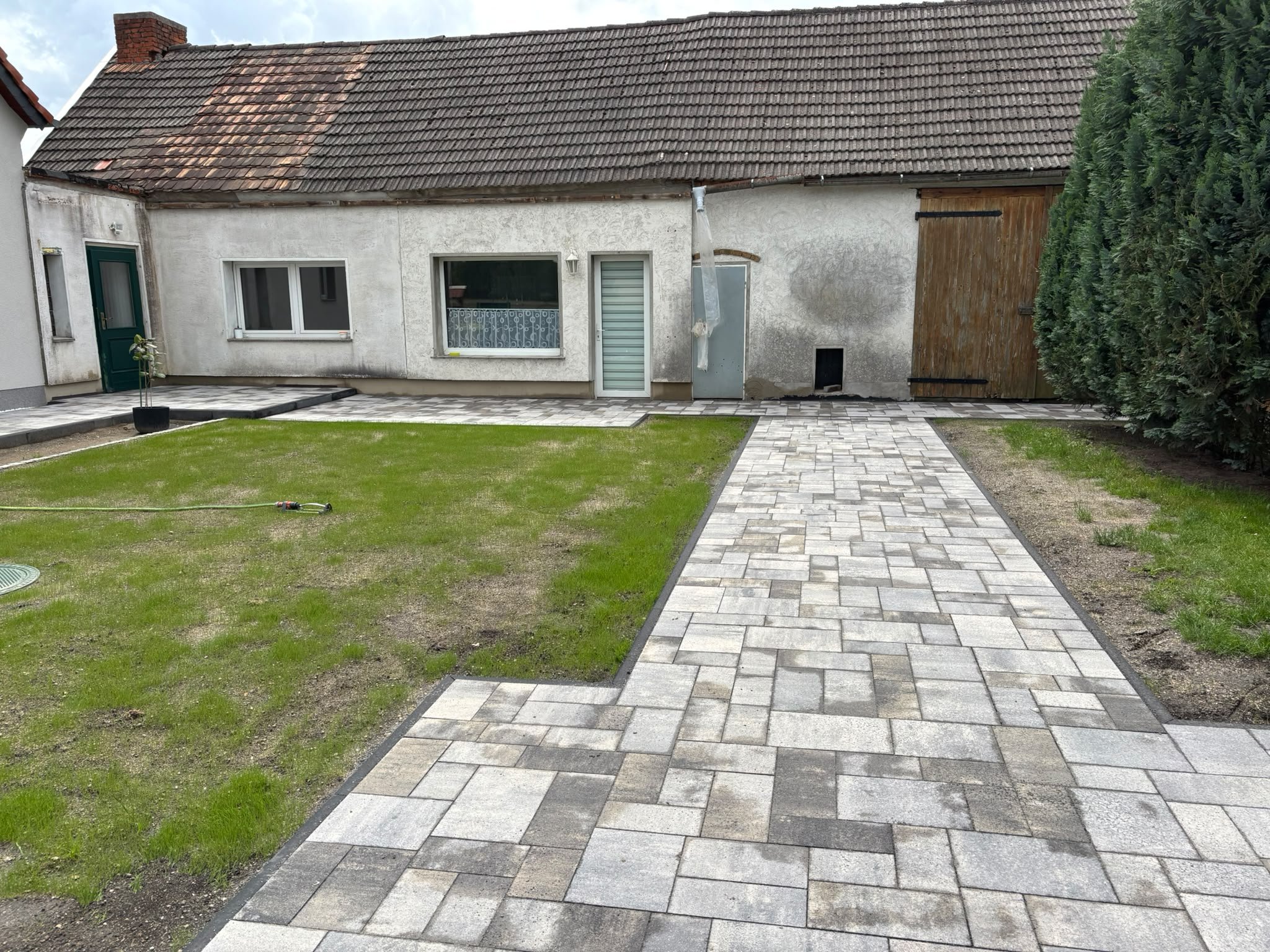 Hof mit neuem Pflasterweg und frisch angelegtem Rasen vor einem Bauernhaus