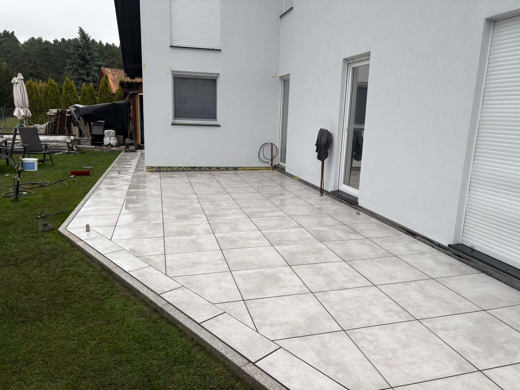 Neue Terrasse aus hellen Keramikplatten an einem weißen Wohnhaus