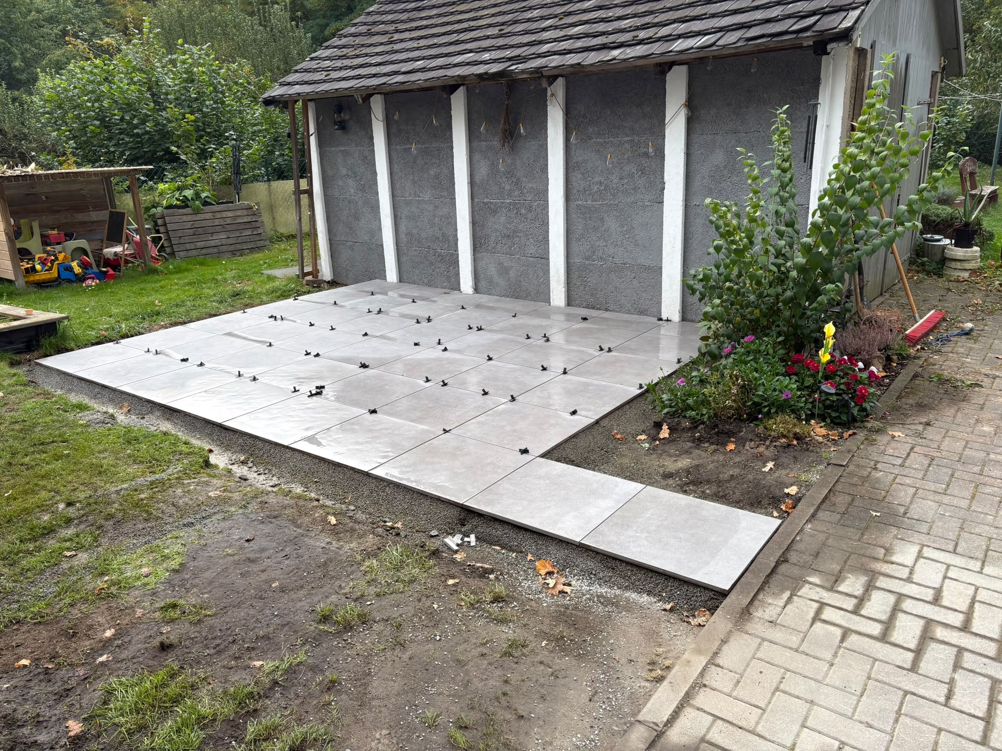 Neu verlegte Keramikplatten vor einem Gartenschuppen, die Fugenkreuze stecken noch