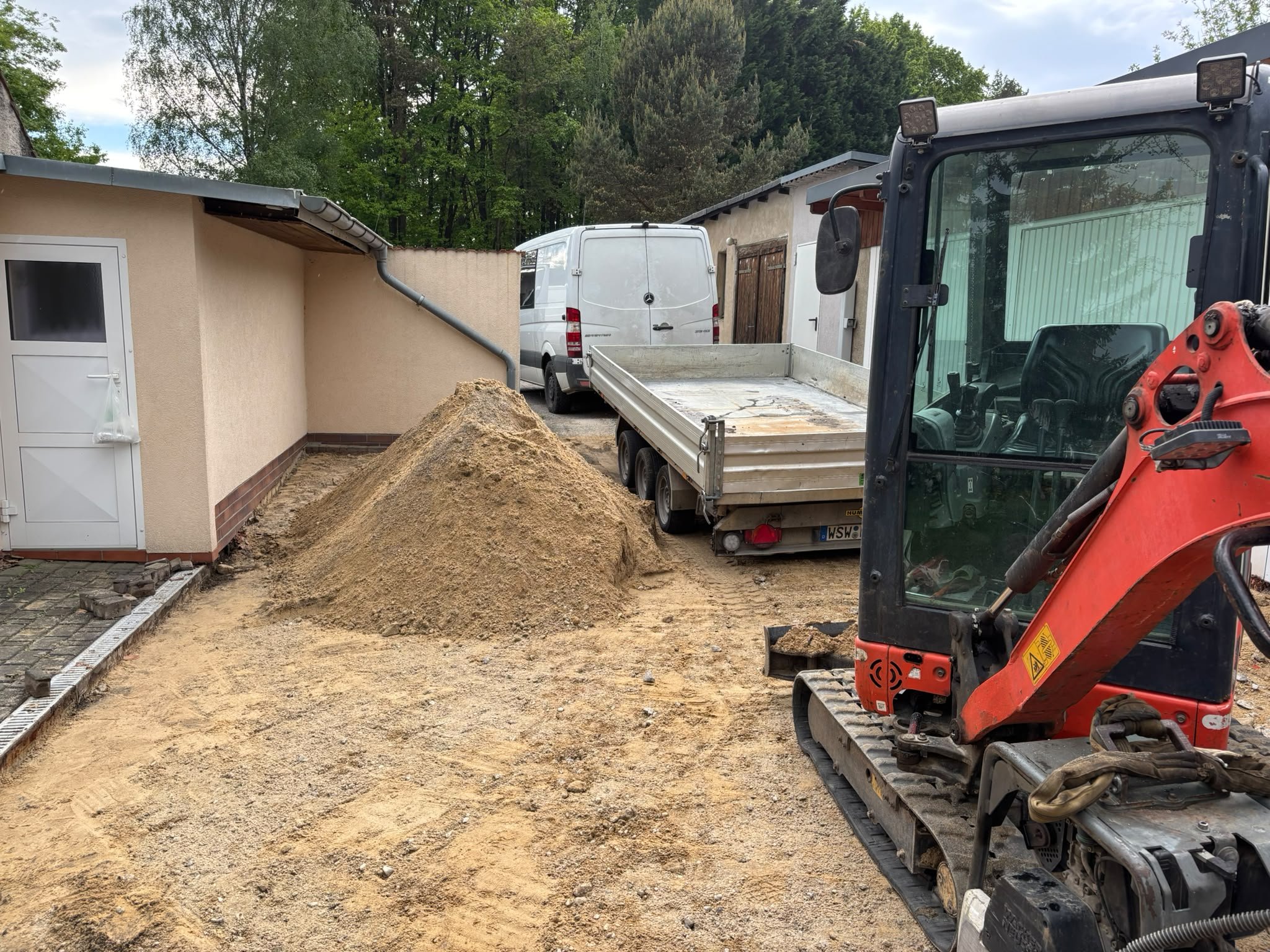 Minibagger und Anhänger bei Erdarbeiten auf einem Hof