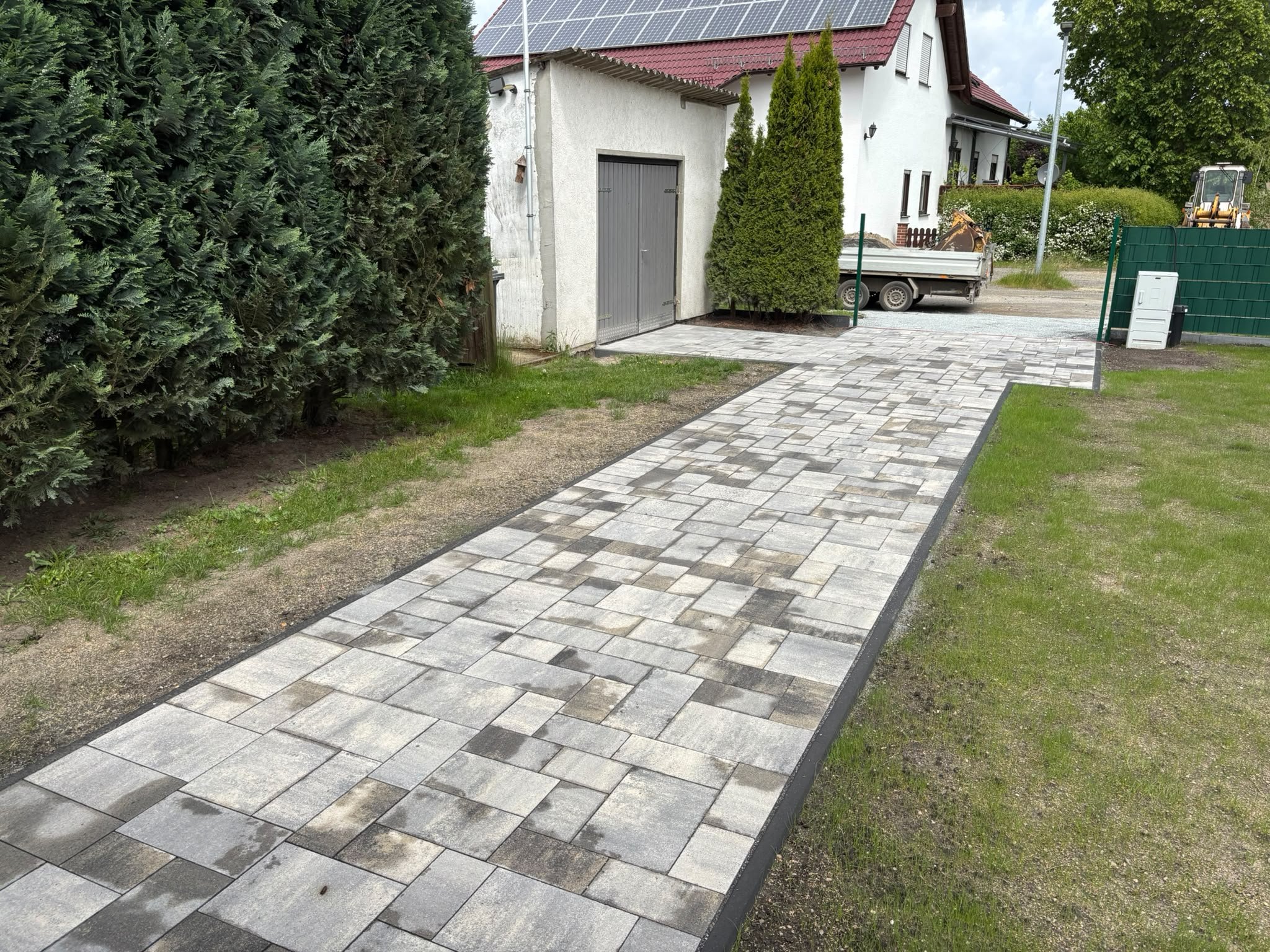 Neuer Pflasterweg mit Rasenstreifen neben einer hohen Hecke
