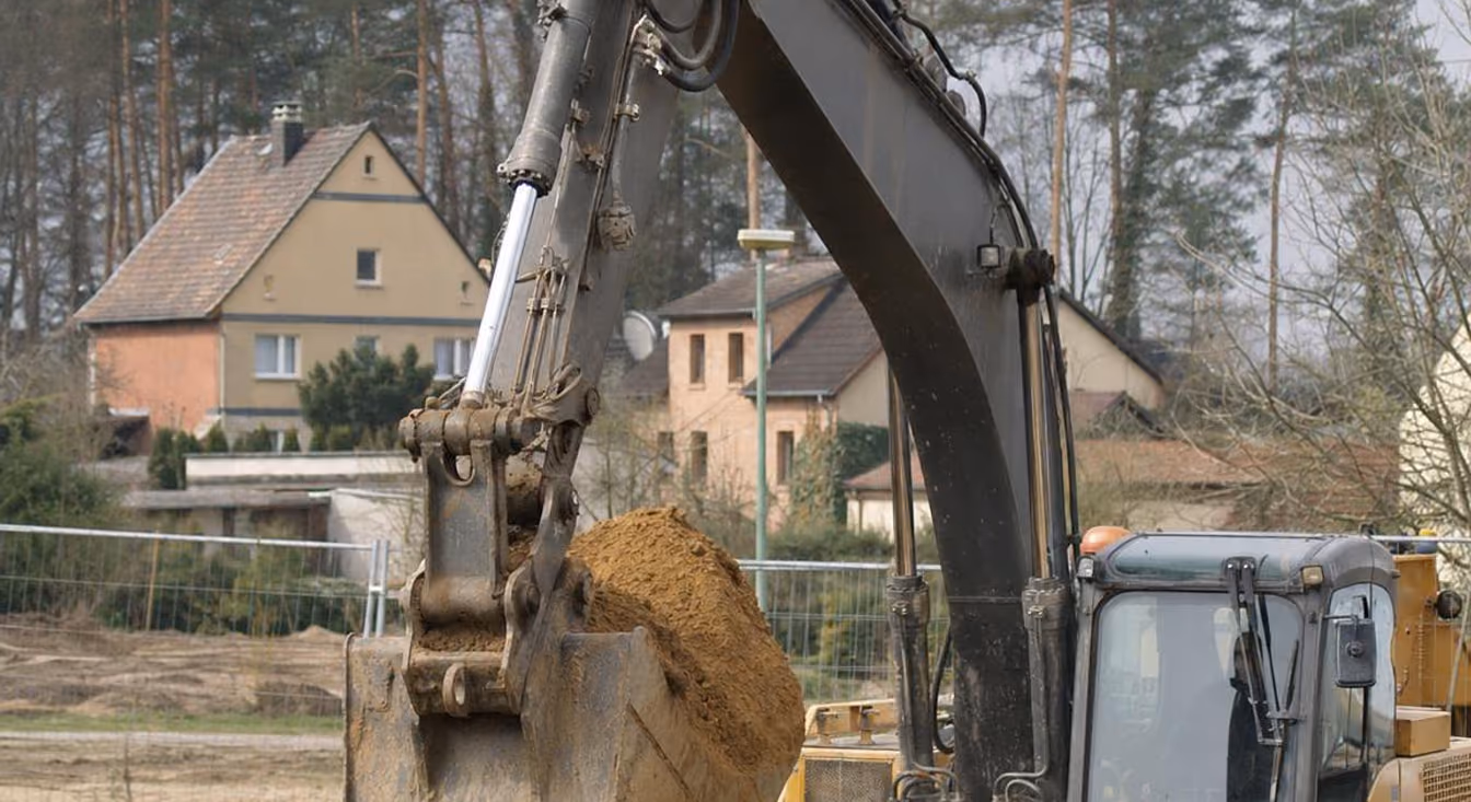 Kettenbagger hebt eine Schaufel mit sandigem Boden aus einer Baugrube
