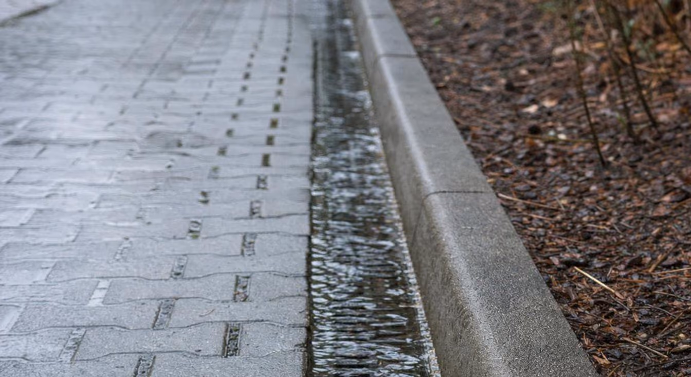 Nasse Pflasterfläche mit Entwässerungsrinne und Randstein nach einem Regenschauer