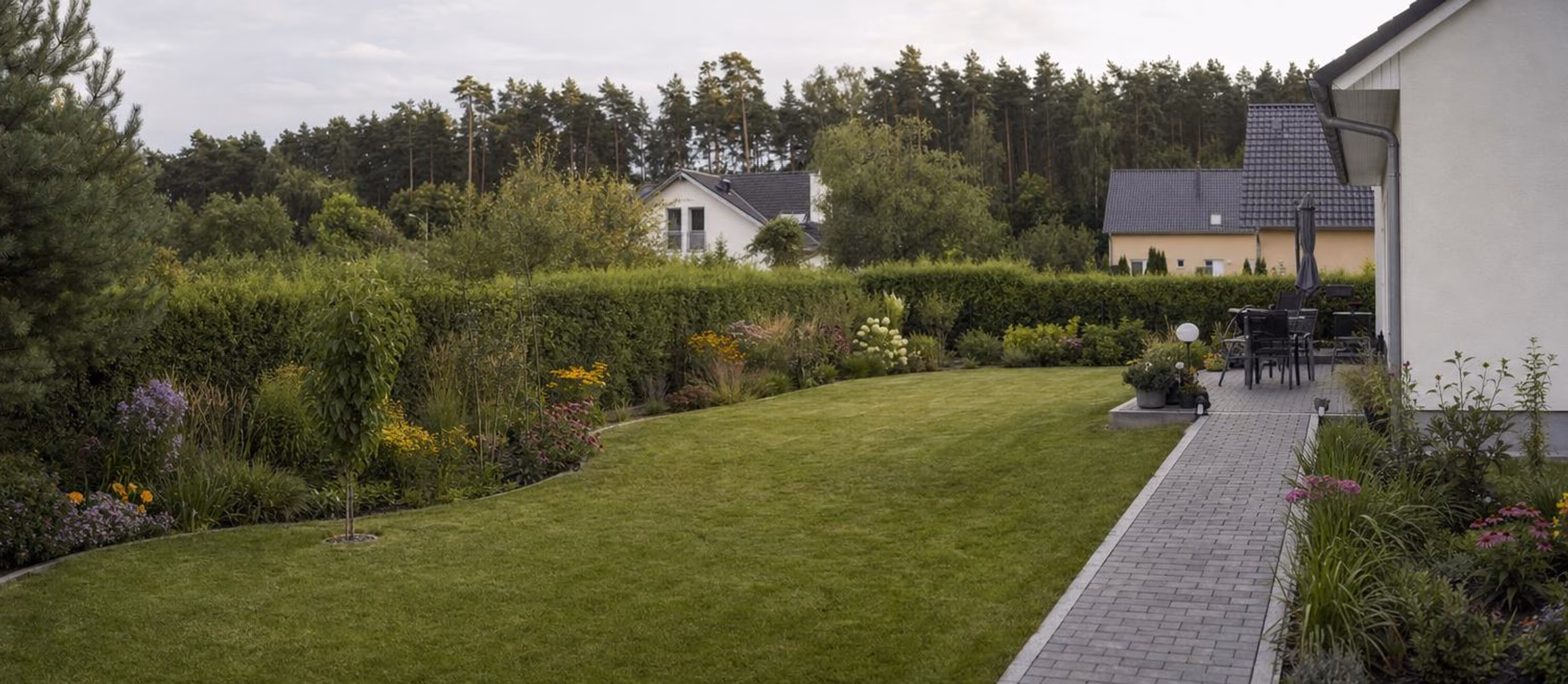 Gepflasterter Weg durch einen Garten zu einer kleinen Plattenterrasse am Haus