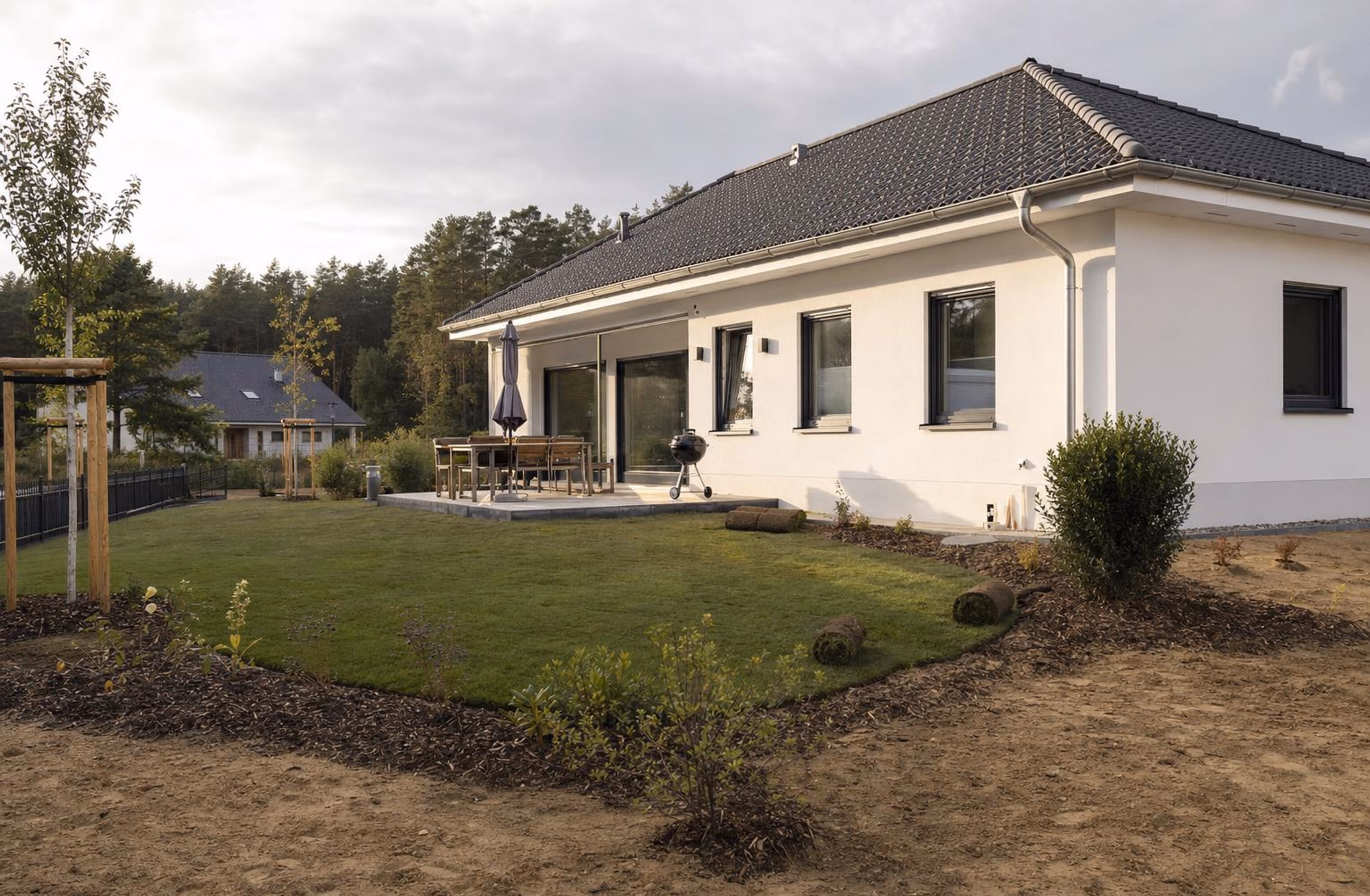 Neubau mit frisch verlegtem Rollrasen, Plattenterrasse und jungen Bäumen