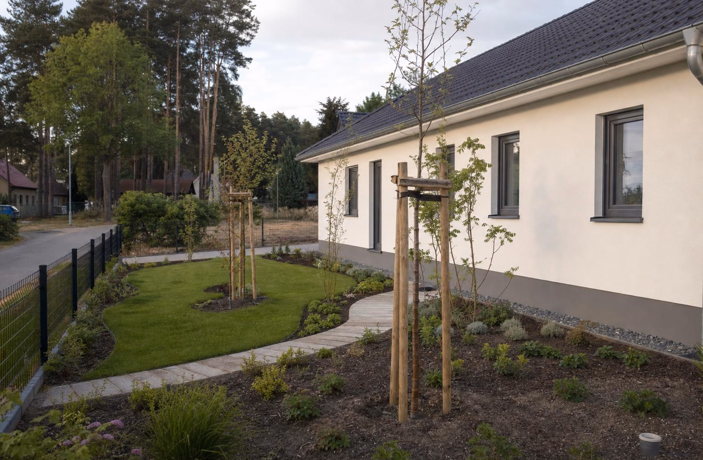Frisch angelegter Garten mit geschwungenem Rasen, Beeten und Pflasterweg vor einem Neubau